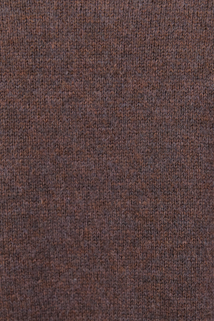 Woman wearing a chocolate brown knit jumper and blue jeans against a white background