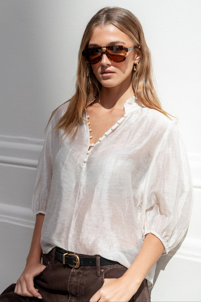 Woman wearing a white blouse and sunglasses against a light background