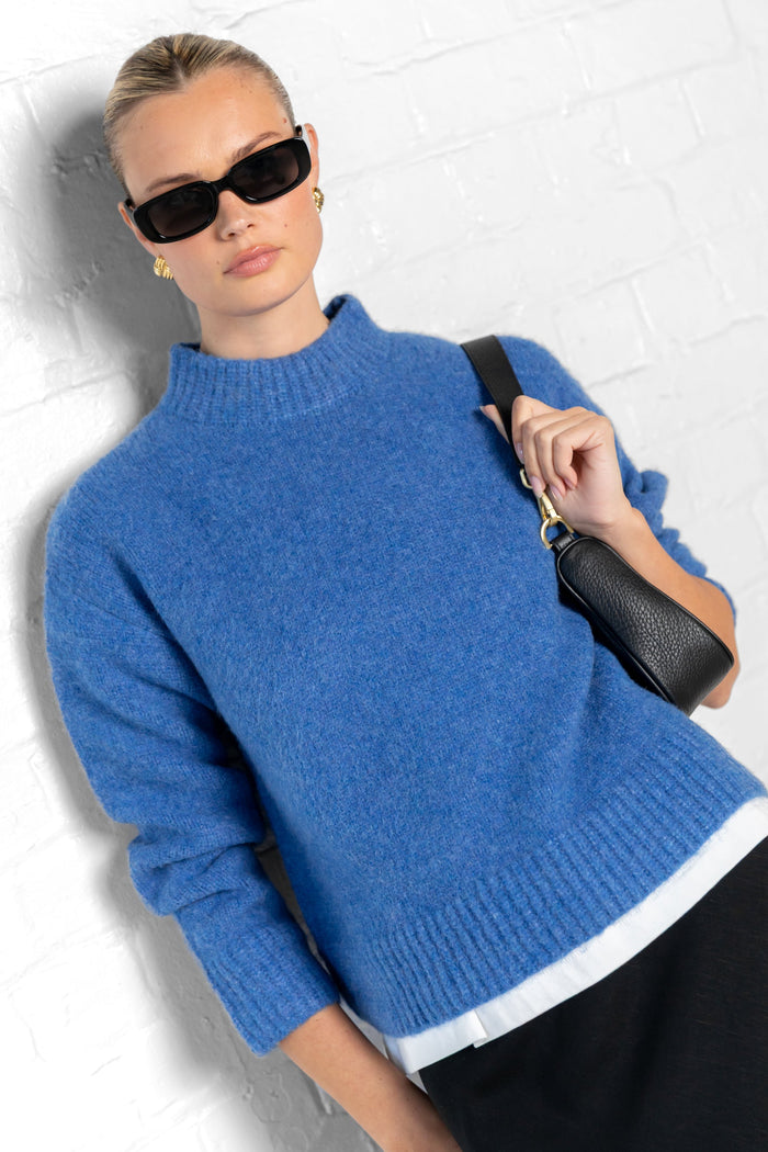 Woman wearing a blue sweater and sunglasses against a white background