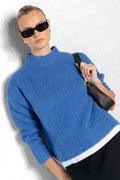 Woman wearing a blue sweater and sunglasses against a white background
