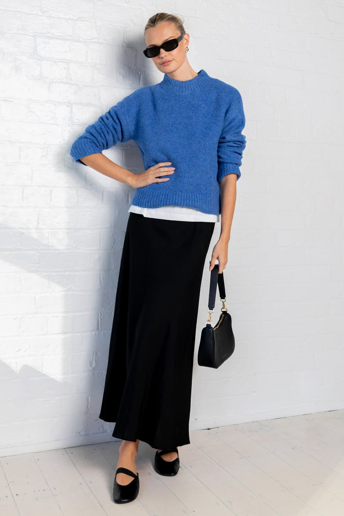 Person wearing a blue sweater and black skirt with sunglasses indoors.