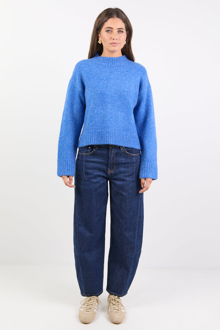 Person wearing a blue sweater and dark jeans on a white background