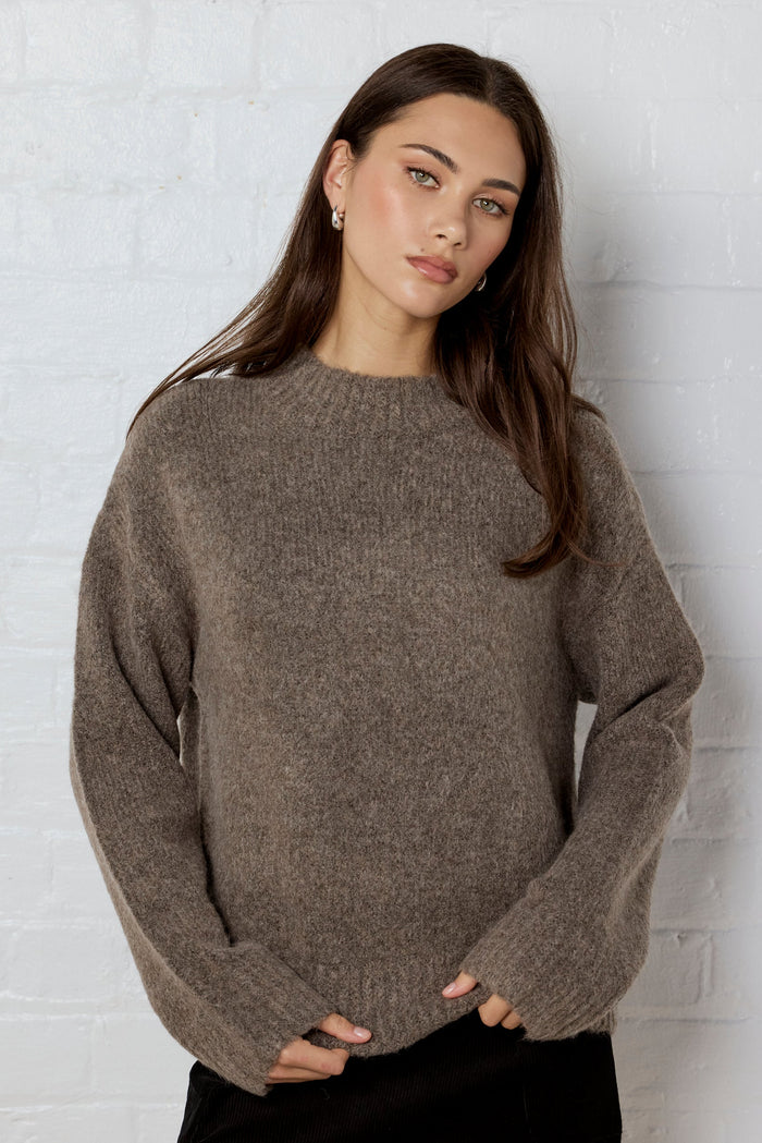 Woman wearing a brown sweater against a white brick wall