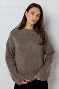 Woman wearing a brown sweater against a white brick wall