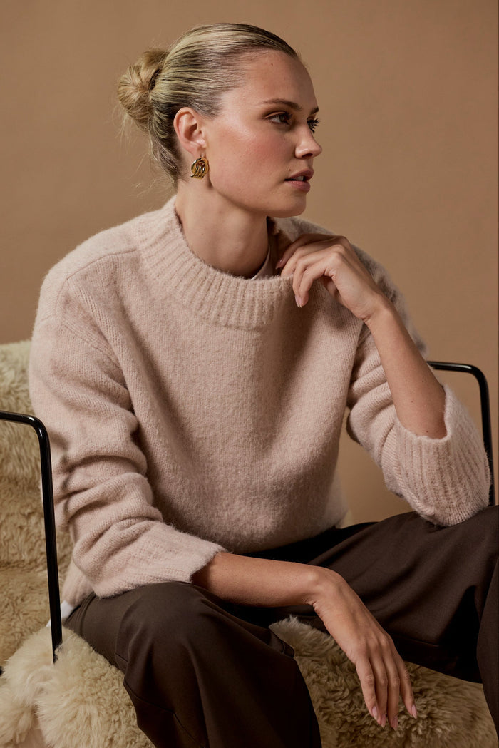 Woman wearing a beige sweater sitting on a textured surface with a neutral background
