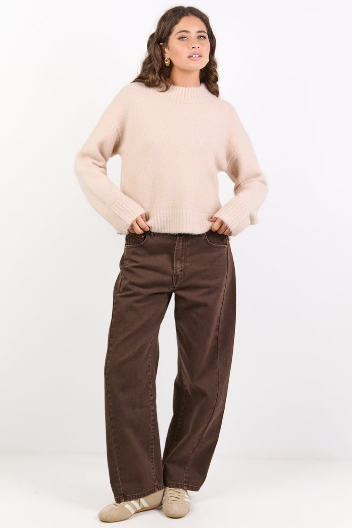 Woman wearing a beige sweater and brown pants on a white background