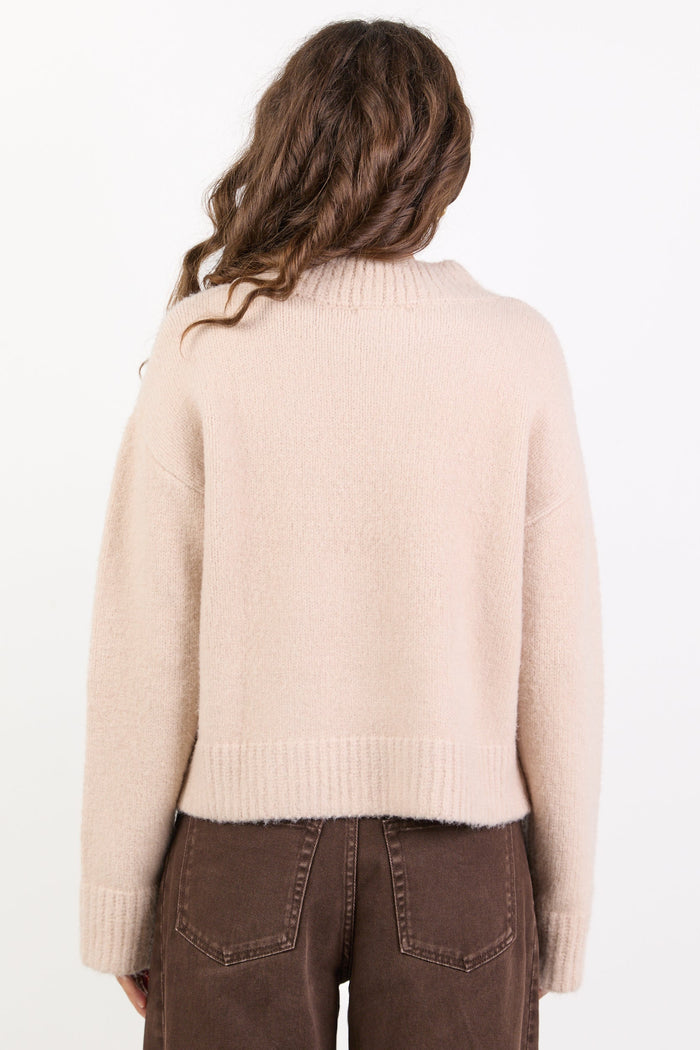 Person wearing a beige sweater and brown pants on a white background