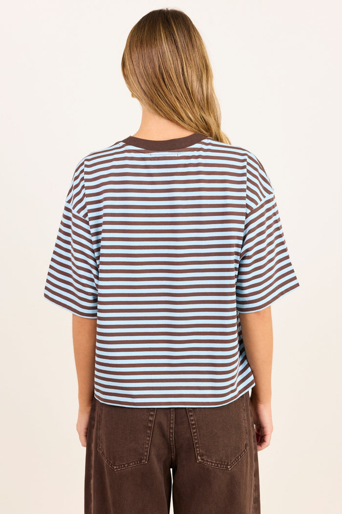 A woman viewed from behind wearing a brown and white horizontally striped short-sleeve t-shirt and brown pants, set against a plain off-white background.
col_pattern