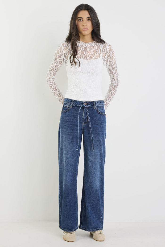Woman wearing a white lace top and blue jeans on a white background