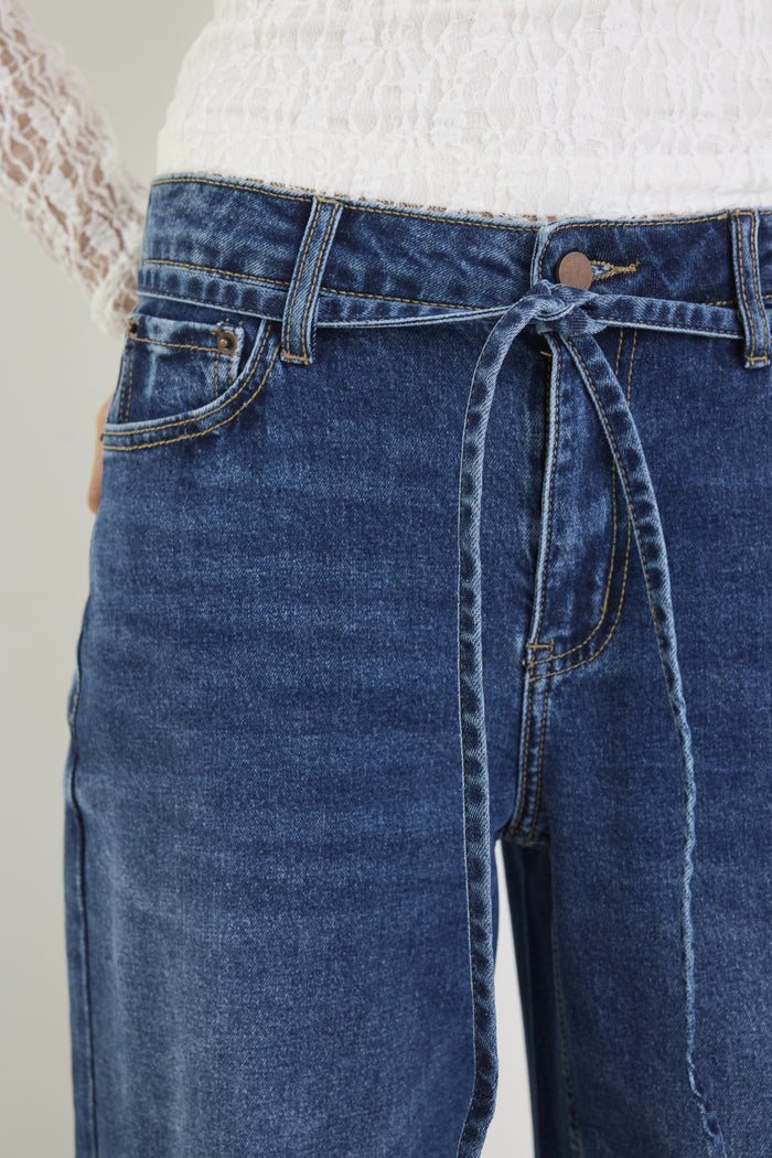 Blue jeans with a tie-waist design on a plain background