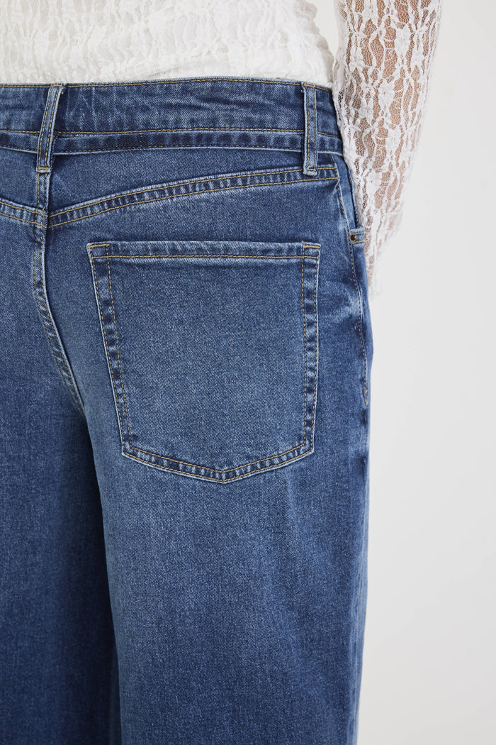 Close-up of blue jeans with a white lace garment in the background