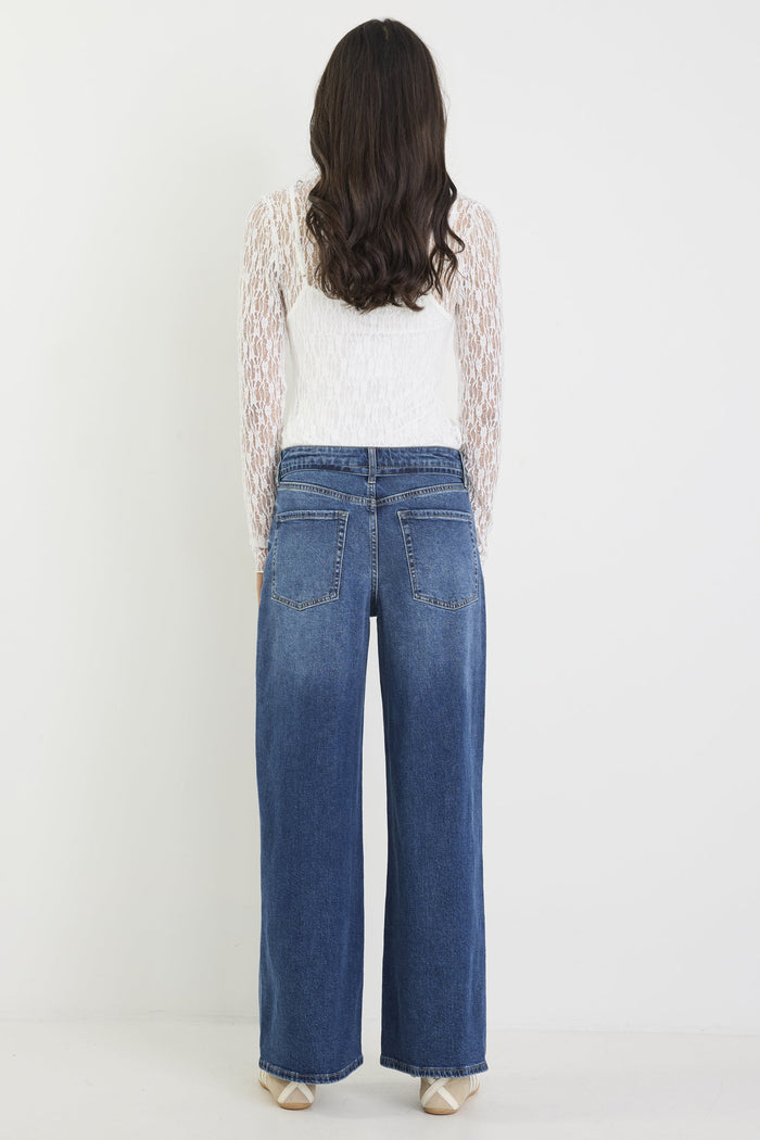 Person wearing blue jeans and a white top with lace sleeves on a white background
