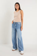 Woman wearing a beige sleeveless top and light blue jeans on a white background