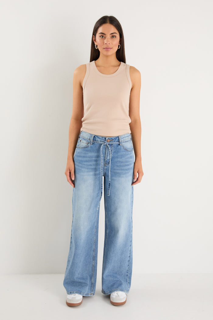 Woman wearing a beige sleeveless top and light blue jeans on a white background
