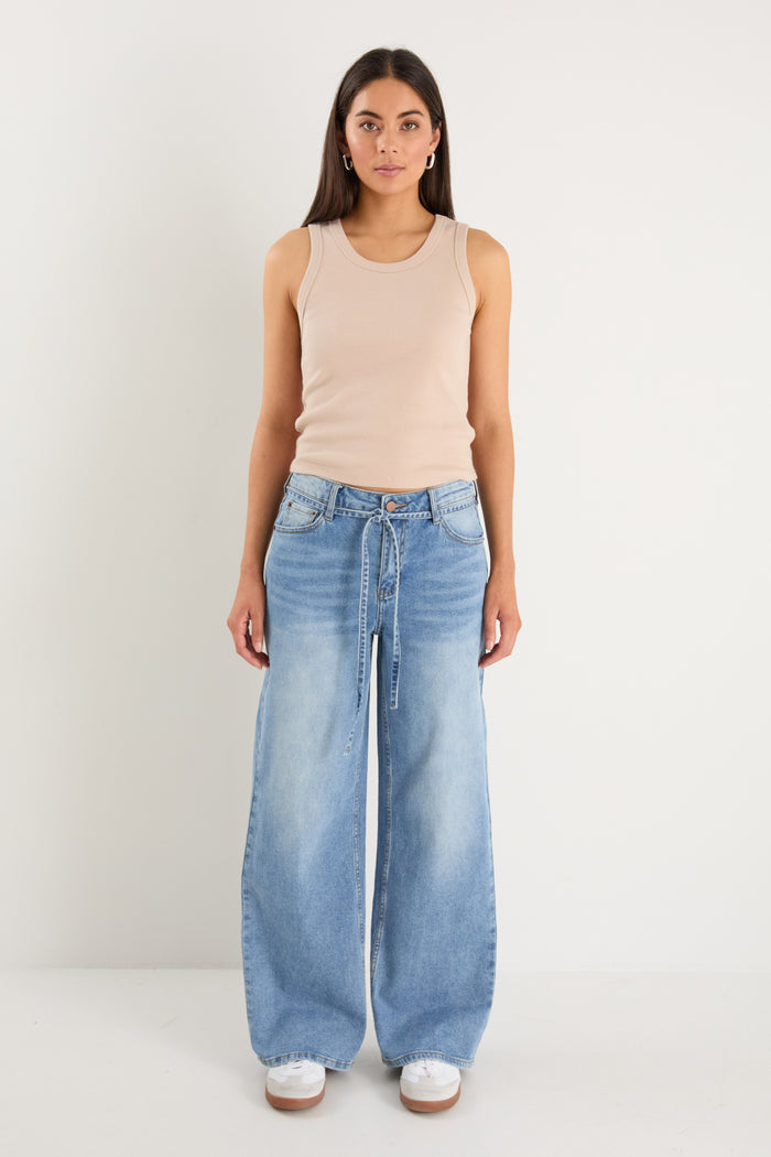 Woman wearing a beige tank top and light blue jeans on a white background