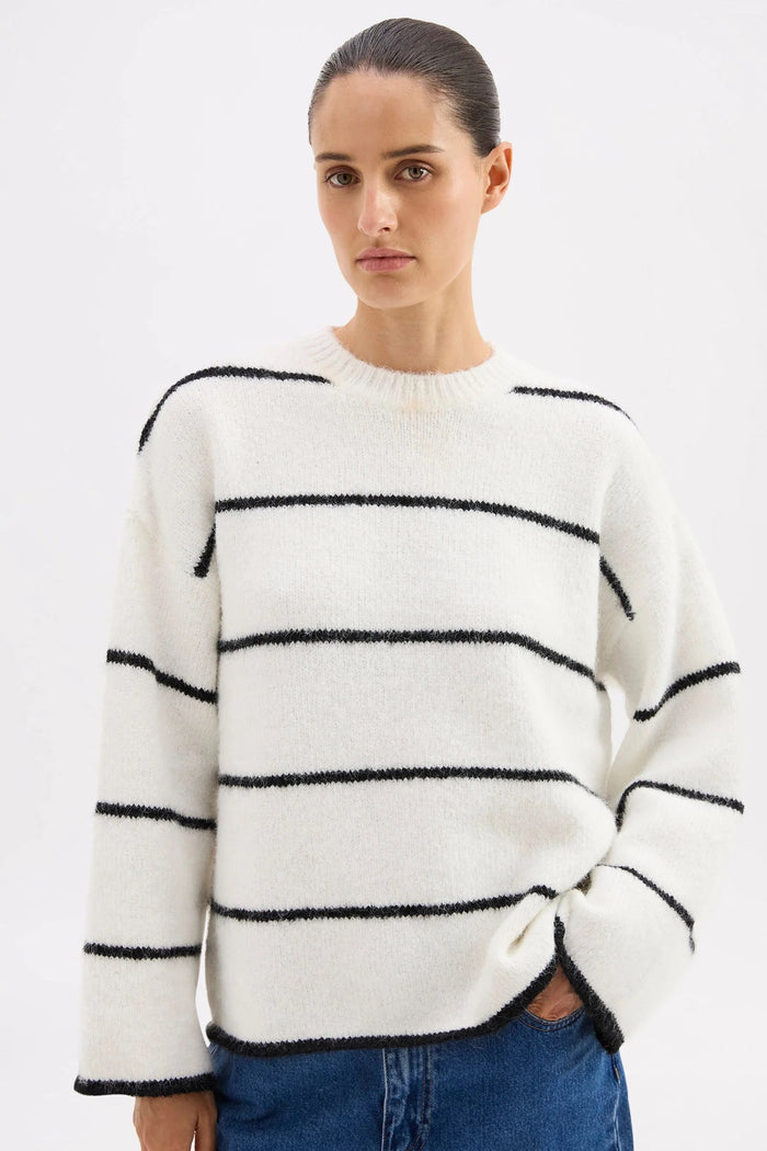 Woman wearing a white sweater with black horizontal stripes on a plain background