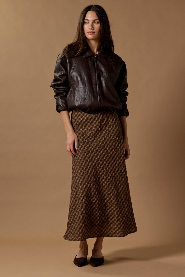 Woman wearing a black leather jacket and patterned skirt against a brown background