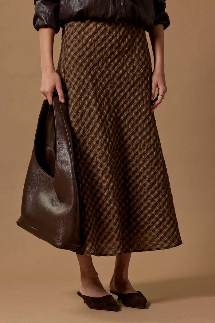 Person wearing a brown houndstooth patterned skirt holding a matching bag against a beige background