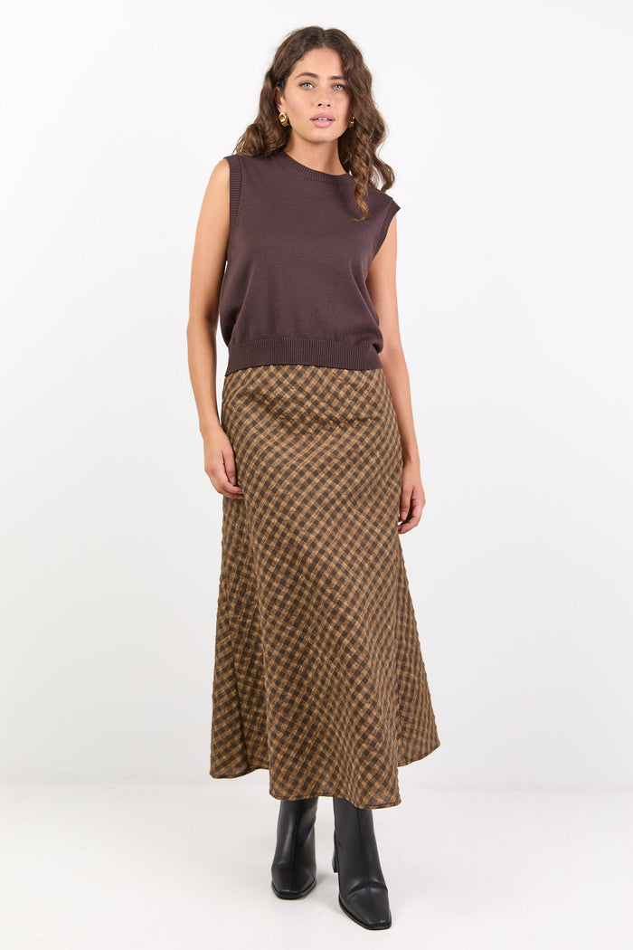 Woman wearing a sleeveless brown top and patterned skirt on a white background