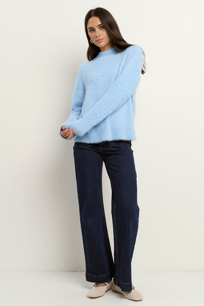 Woman wearing a light blue fuzzy funnel neck knit with relaxed fit and long sleeves, paired with dark wide-leg jeans.