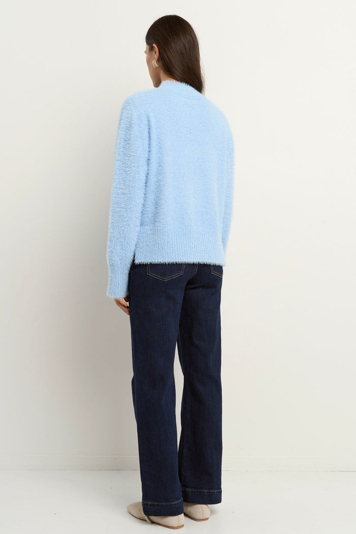 Woman wearing a light blue fuzzy funnel neck knit with relaxed fit and long sleeves, paired with dark wide-leg jeans.