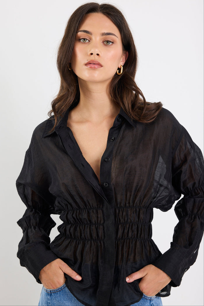 Woman wearing a black sheer blouse with long sleeves on a white background