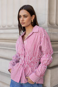 Woman wearing a pink and white striped shirt against a stone wall.