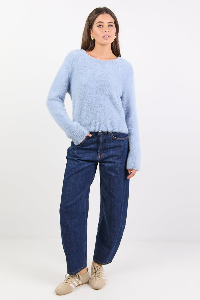 Woman wearing a light blue sweater and dark blue jeans on a white background