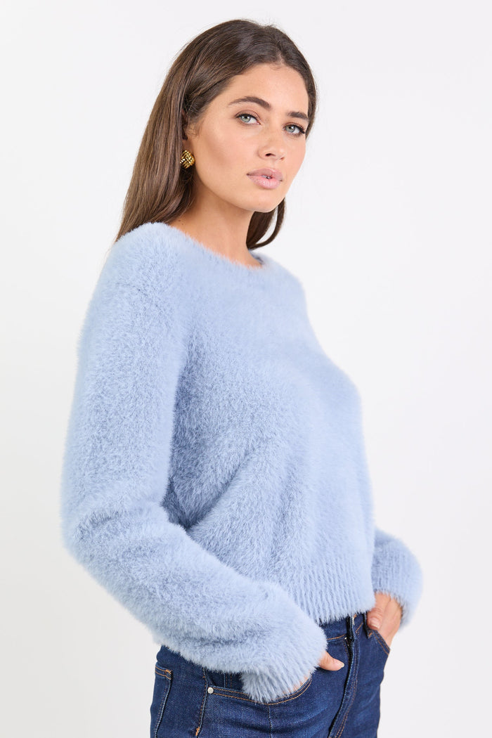 Woman wearing a light blue fuzzy sweater and dark blue jeans on a white background