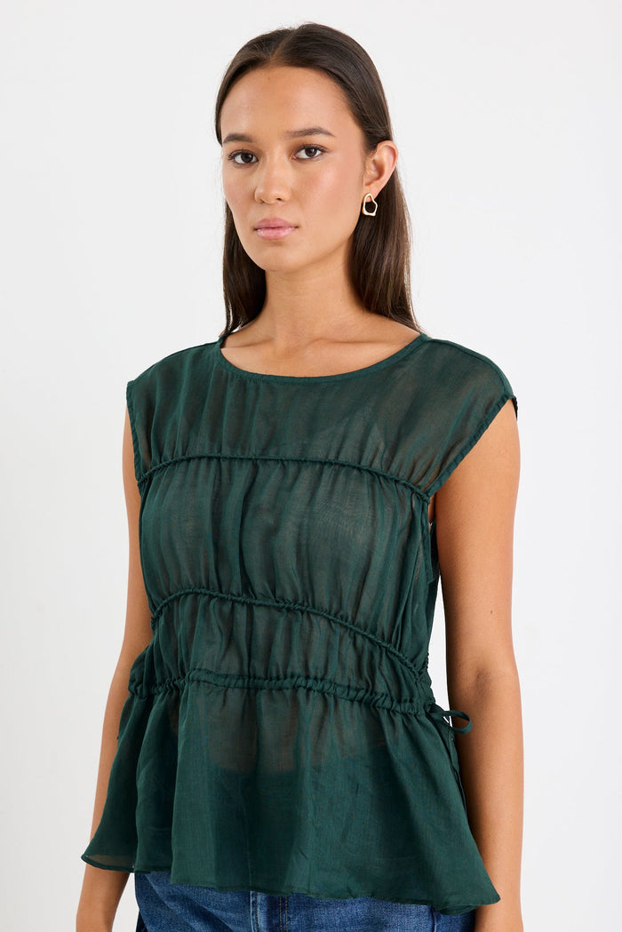 Woman wearing a green sleeveless top and blue jeans on a white background