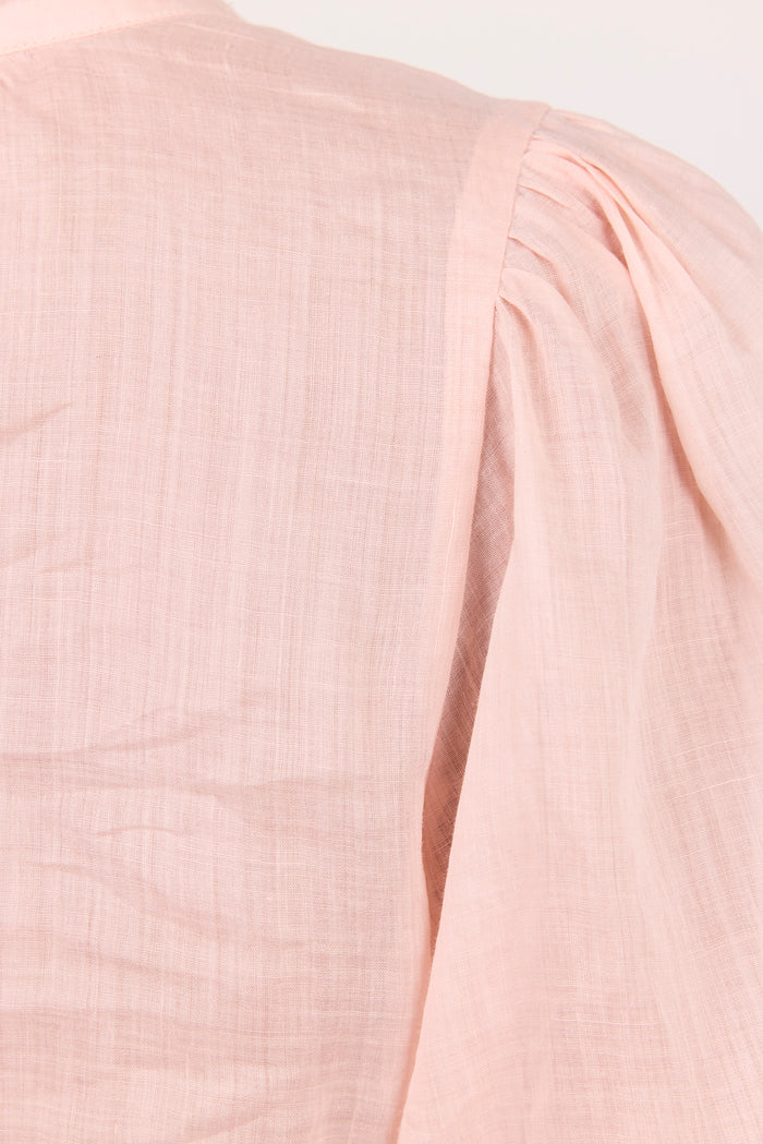 Close-up of a light pink textured fabric garment showing a shoulder seam and pleated detail against a plain light background.
col_pattern