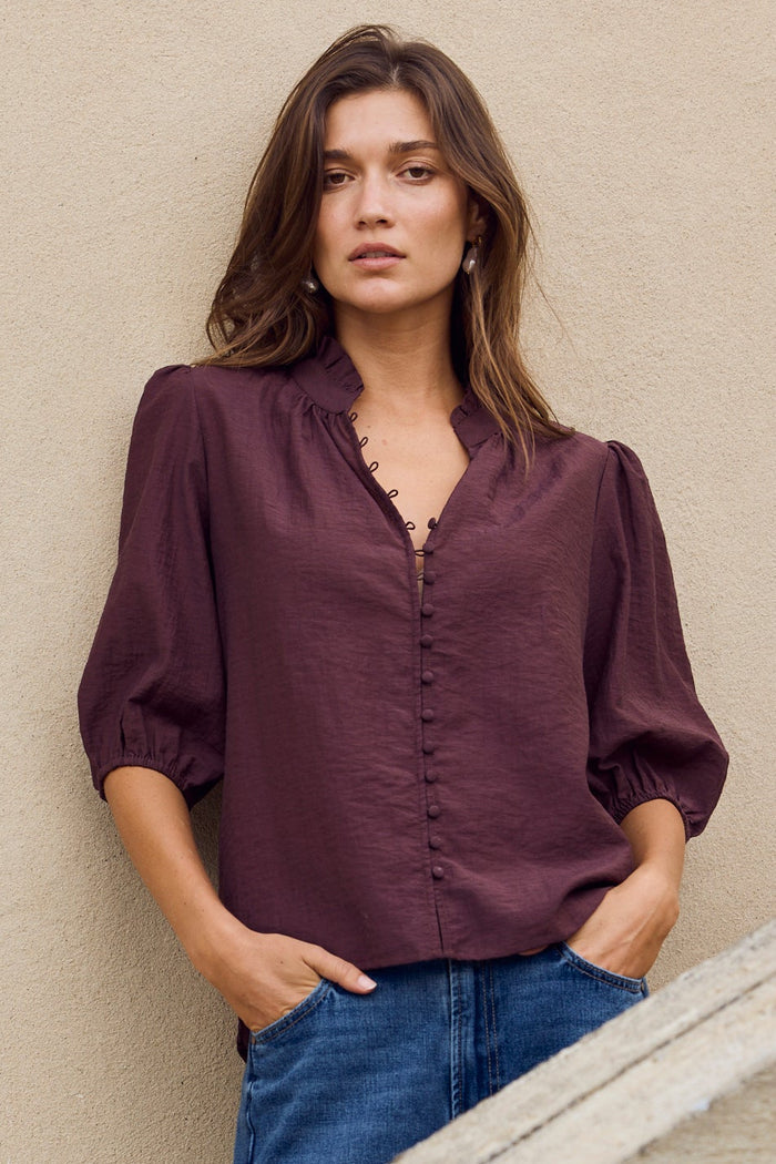 Woman standing against a beige wall with a stone wall in the foreground