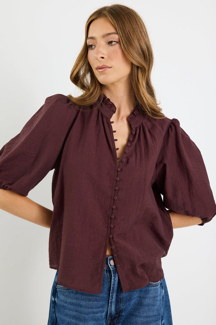 Woman wearing a burgundy blouse with puffed sleeves on a white background