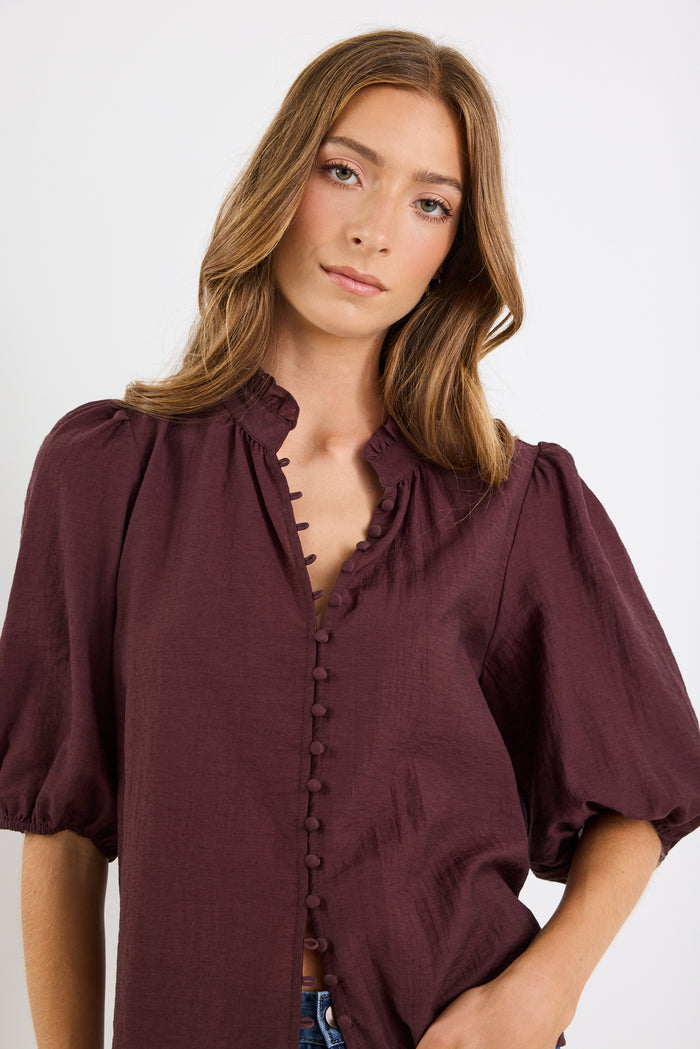 Woman wearing a burgundy blouse with puffed sleeves on a white background