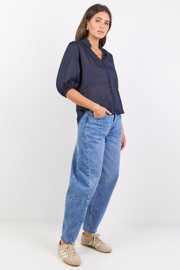 Woman wearing a navy shirt and light blue jeans on a white background
