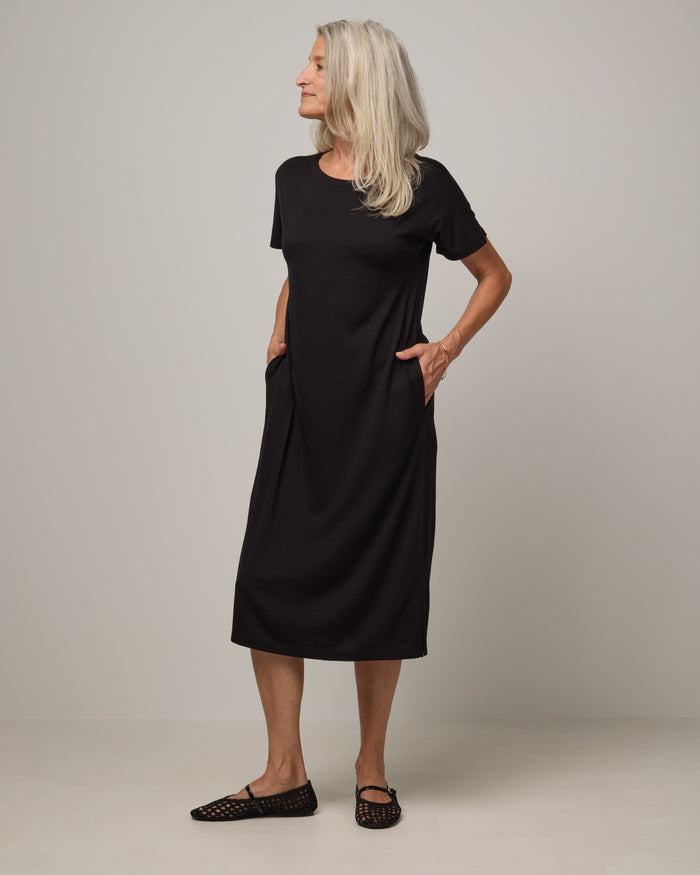 Model wearing Cora Shift Dress in Black. Cora Shift Dress is a merino wool short sleeve, midi shift dress with pockets and removable belt available in sizes XS-3X.