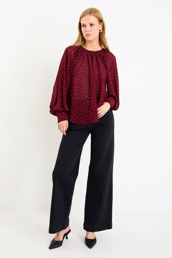 Model wearing a burgundy long sleeve polka dot blouse with a floaty fit, crew neckline and balloon sleeves.