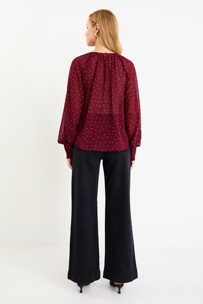 Model wearing a burgundy long sleeve polka dot blouse with a floaty fit, crew neckline and balloon sleeves.