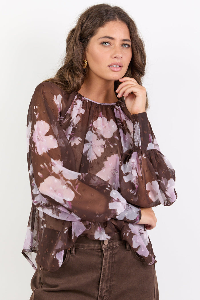 Woman wearing a brown floral blouse against a white background