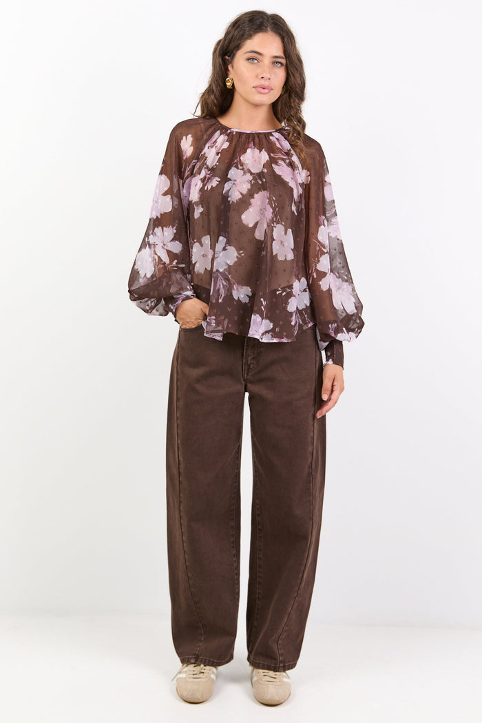 Woman wearing a floral blouse and brown pants on a white background