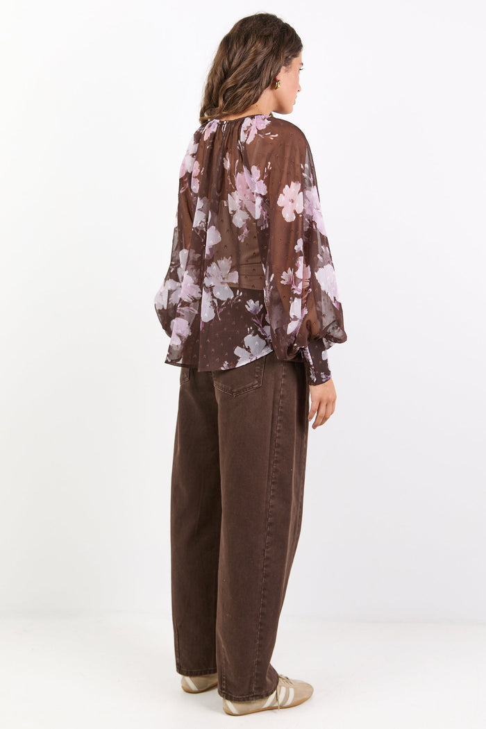 Woman wearing a floral blouse and brown pants on a white background