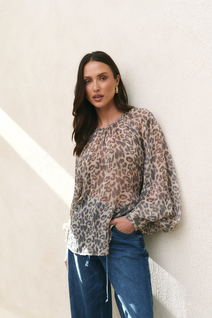 Woman wearing a leopard print blouse and blue jeans against a light background