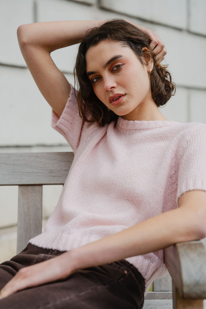 Woman wearing a pink knit sweater sitting on a wooden bench.