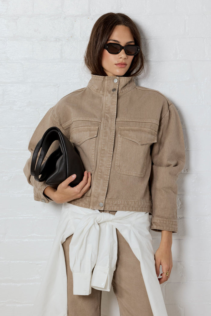 Woman wearing a beige jacket and pants, holding a black clutch against a white background