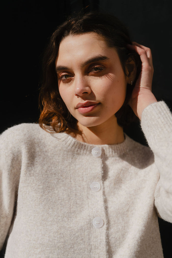 Woman wearing a light gray cardigan against a dark background