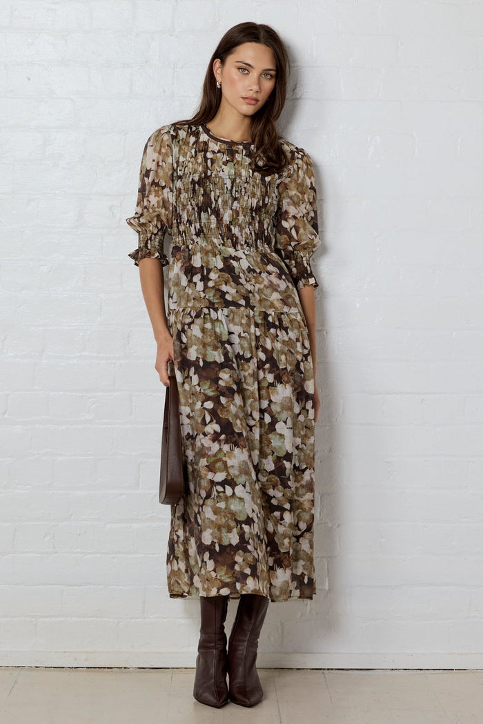 Woman wearing a floral dress against a white brick wall.