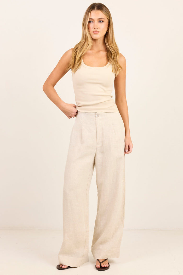 A woman modeling a cream-colored sleeveless tank top and matching wide-leg linen pants against a plain off-white studio background.