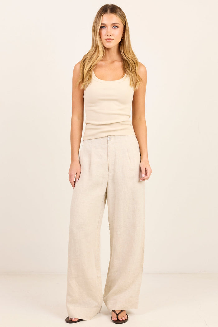 A woman modeling a light beige ribbed tank top and matching wide-leg linen pants against a clean, off-white studio background.