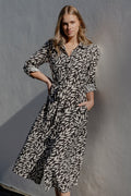 Woman in a patterned dress standing against a plain wall