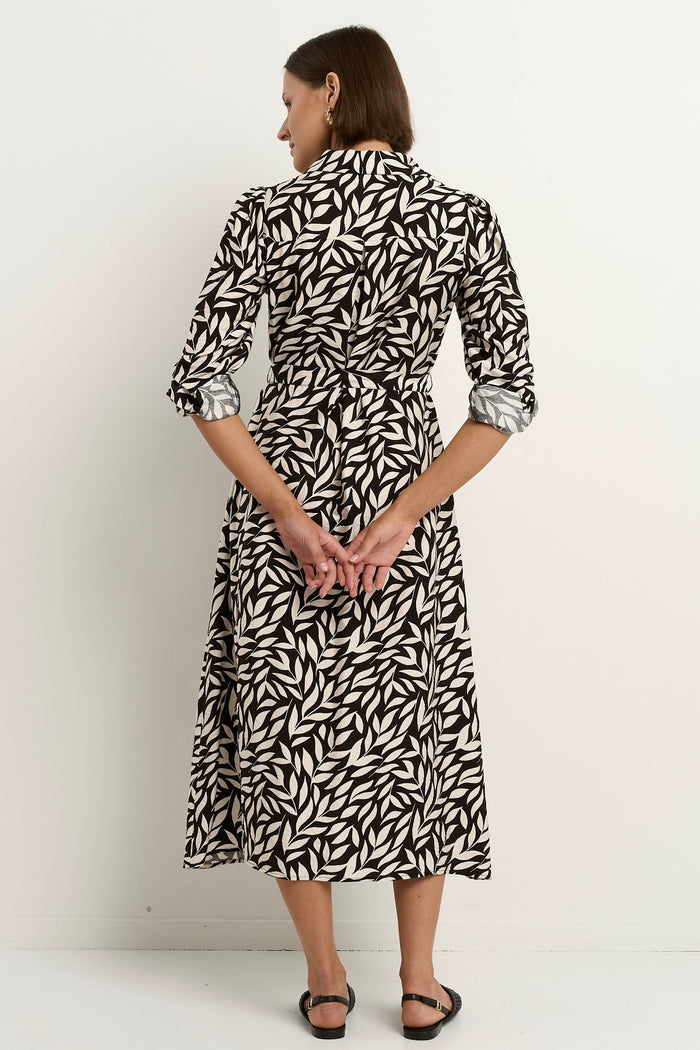 Woman wearing a black-and-white leaf-print midi dress with a relaxed button-down design and long sleeves, styled with black woven flats.